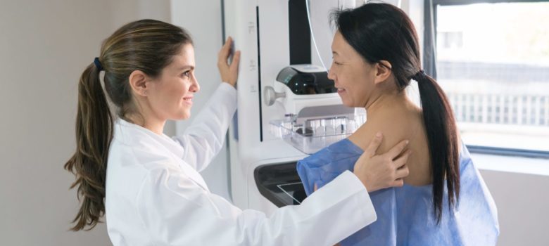 Female gynecologist helping a patient get in position for a mammogram both looking happy and smiling